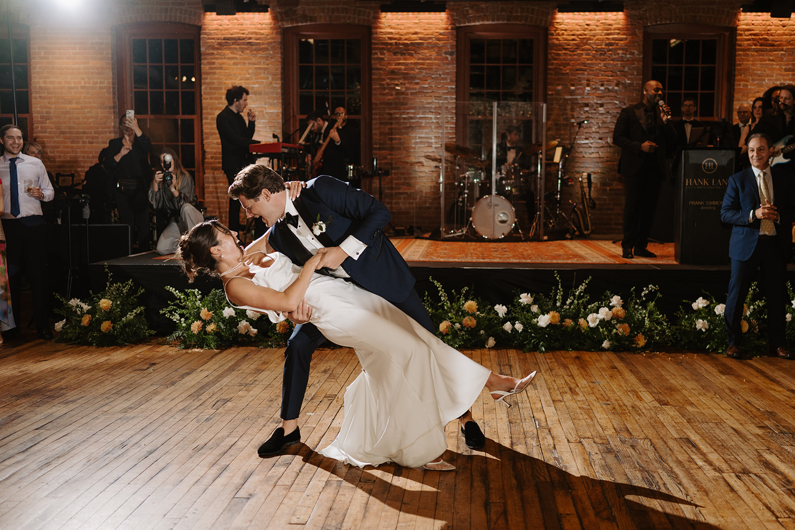 First dance in front of the live band on the stage at City Winery Hudson Valley, brick walls and florals along the stage front, Montgomery NY